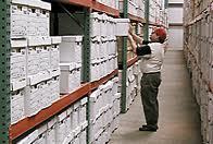 person searching wall of file boxes